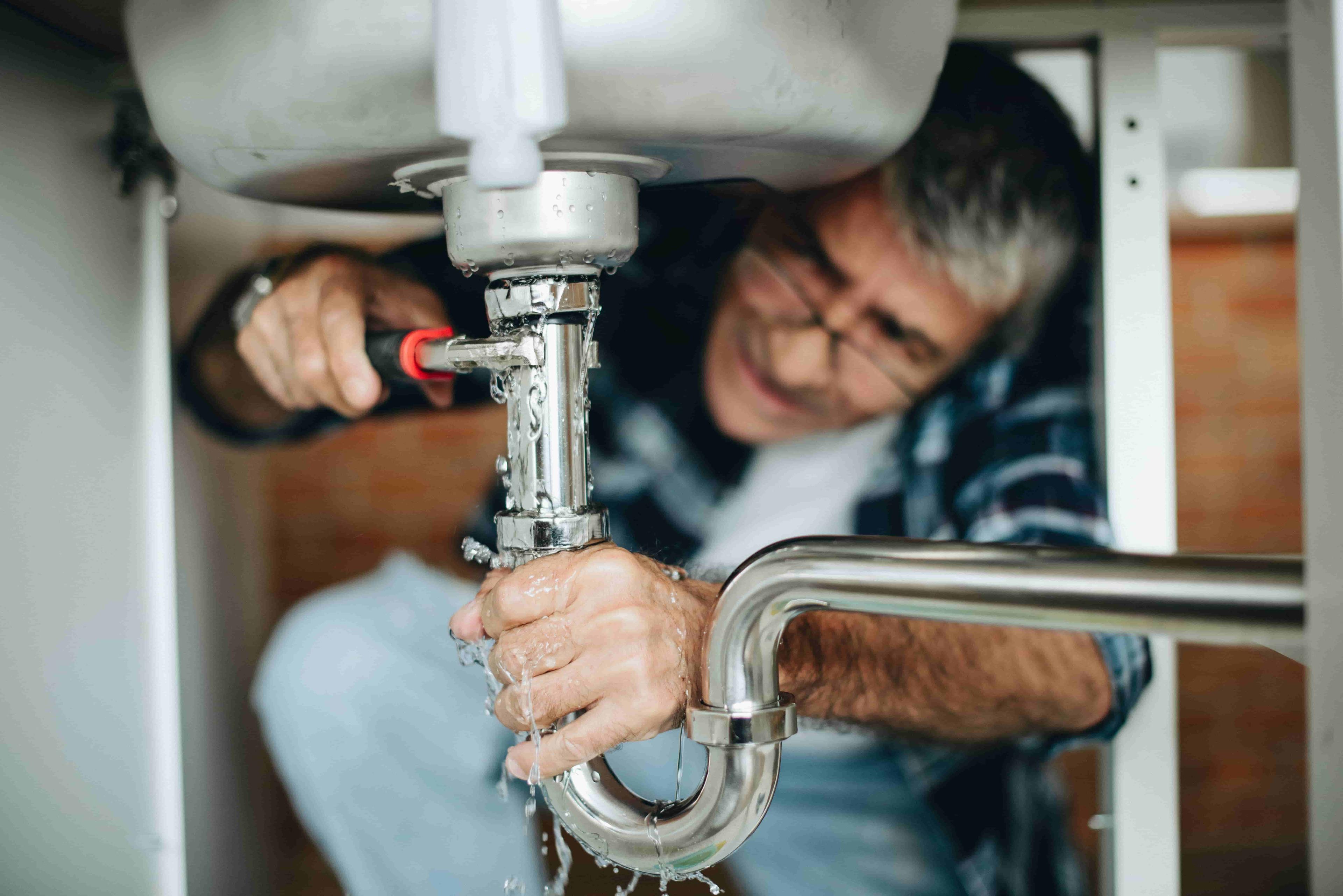 Homeowner struggling to DIY fix a leaking pipe underneath his kitchen sink.