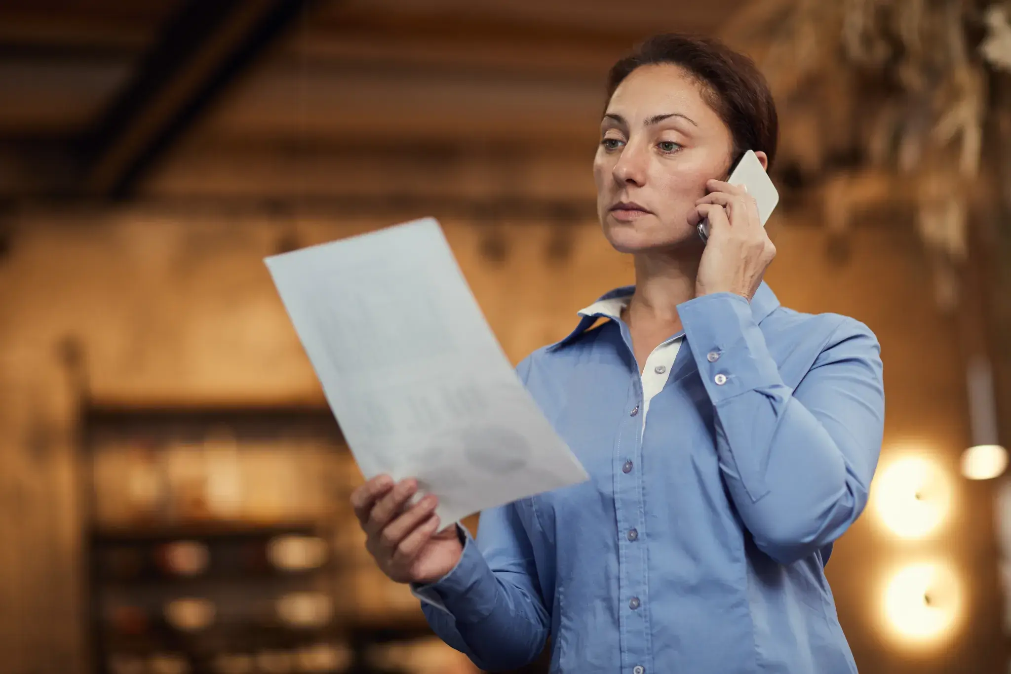 A woman holding a piece of paper and using a phone